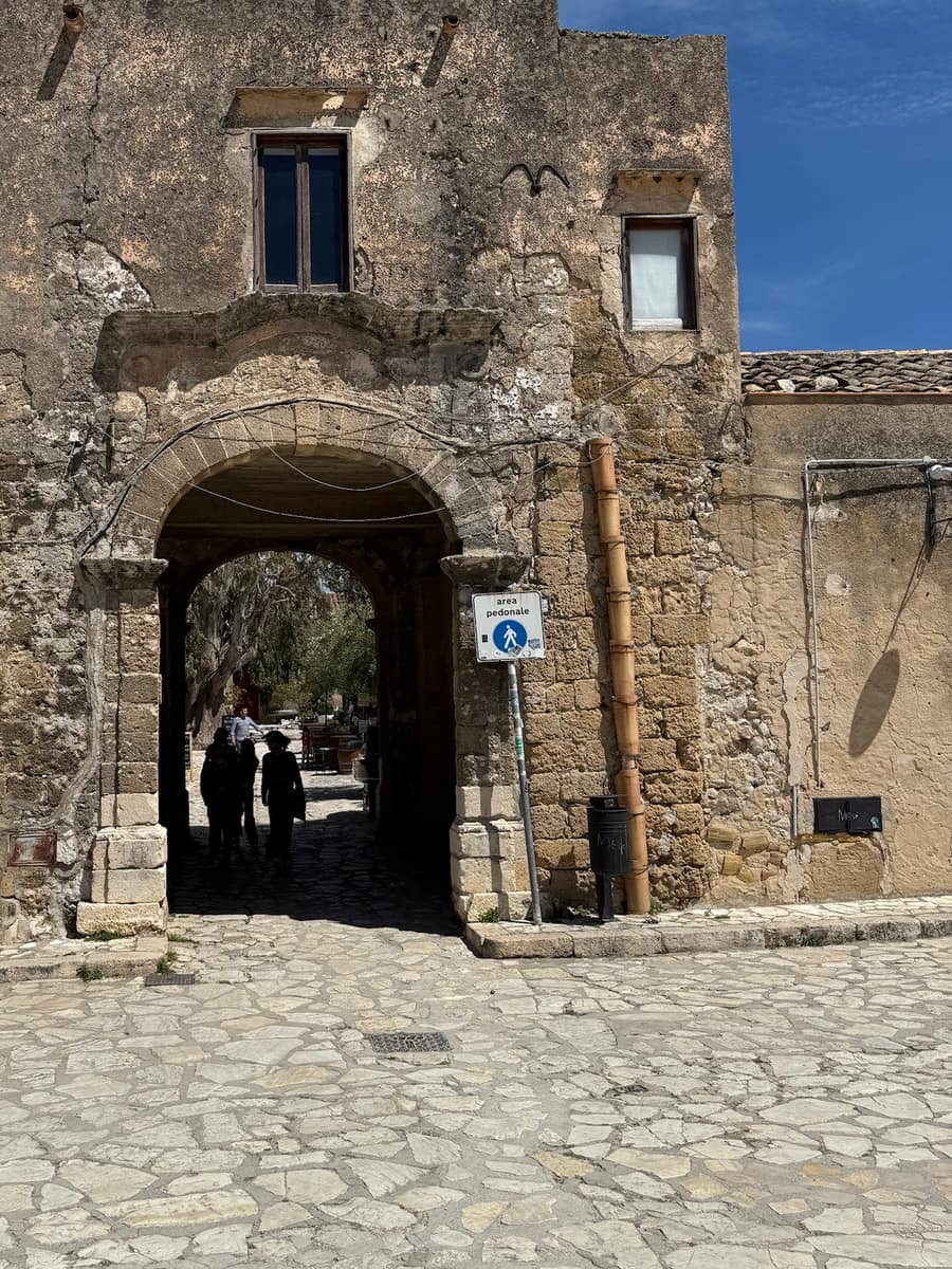 Grande arco in pietra di un edificio antico, con il cartello di area pedonale e la via del borgo visibile oltre l’arcata